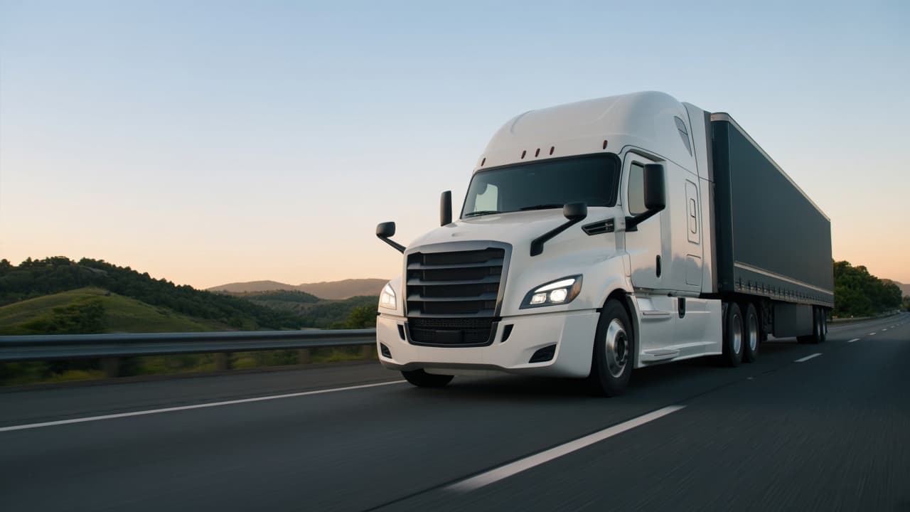 White semi-truck driving on an open highway at sunrise